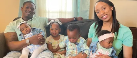 A man and a Woman sitting on a couch with 4 young children.